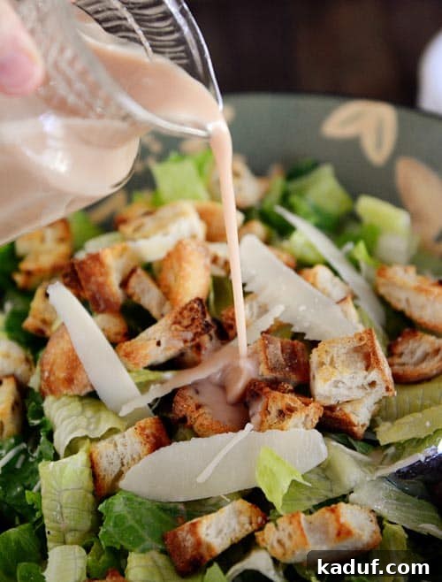 Gourmet Caesar Salad with Homemade Dressing 2 Dressing getting poured over a large bowl of ceasar salad.
