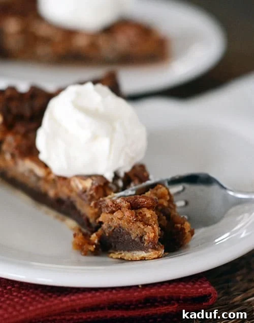 Decadent Chocolate Caramel Pecan Bliss 2 A glorious slice of chocolate caramel pecan pie, adorned with a delicate dollop of whipped cream on top, and a fork poised to take a delicious bite.