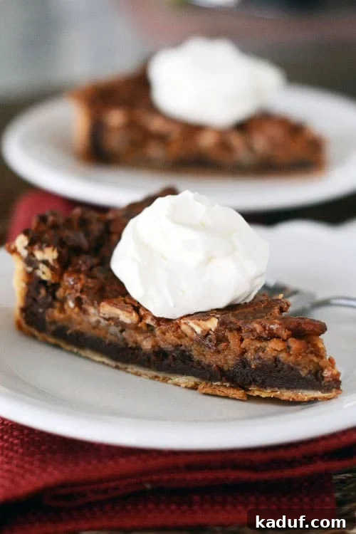 Decadent Chocolate Caramel Pecan Bliss 4 A white ceramic plate holds a perfect slice of chocolate caramel pecan pie, elegantly topped with a dollop of fluffy whipped cream.