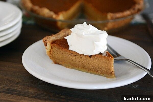 Simply Perfect Pumpkin Pie 5 A pristine slice of classic pumpkin pie, artfully topped with a swirl of sweetened whipped cream, ready to be enjoyed.