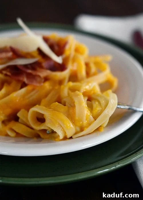 Creamy Butternut Squash Pasta with Crispy Bacon 2 A white plate with cooked linguine pasta topped with bacon and parmesan cheese, highlighting the creamy butternut squash sauce.