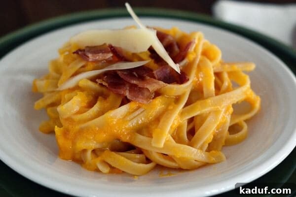 Creamy Butternut Squash Pasta with Crispy Bacon 3 A white plate of butternut squash pasta with chopped bacon and parmesan on top, ready to be served.