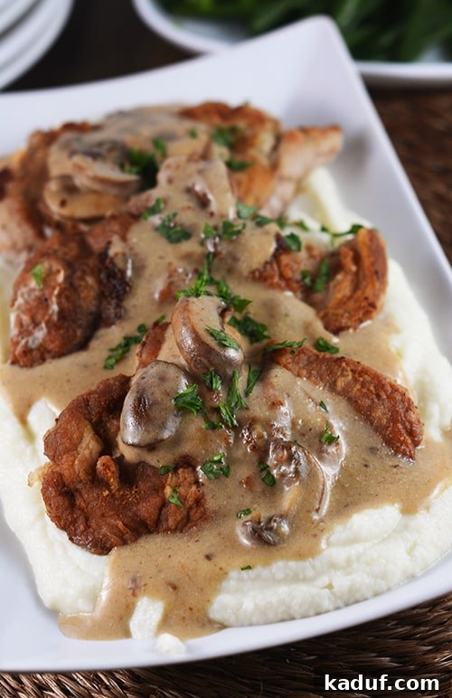 Crispy pork cutlets served over creamy mashed potatoes, generously covered in a rich mushroom gravy, garnished with fresh herbs.