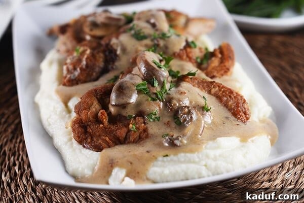 Close-up of crispy pork cutlets arranged on a bed of fluffy mashed potatoes, drenched in a rich, dark brown mushroom sauce.