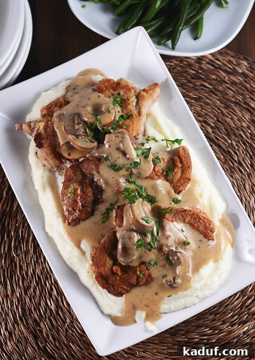 Golden-brown crispy pork cutlets topped with a generous serving of mushroom gravy, resting on creamy mashed potatoes, garnished with fresh parsley.
