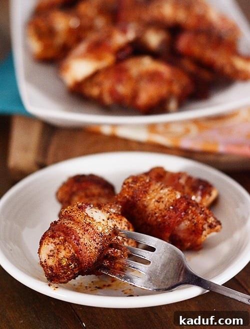 Crispy Bacon Wrapped Chicken Bites 3 A fork picking up a bacon-wrapped chicken bite off of a plate of bites, showing the crispy bacon and moist chicken.