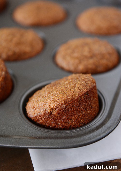 Hearty Honey Bran Muffins 2 Golden brown whole grain honey bran muffins neatly arranged in a muffin tin, with one slightly tilted to show its inviting texture.