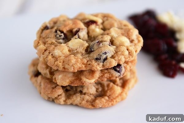 Decadent White Chocolate Craisin Coconut Oatmeal Cookies 2 A stack of three perfectly baked white chocolate craisin cookies, showcasing their soft, chewy texture.