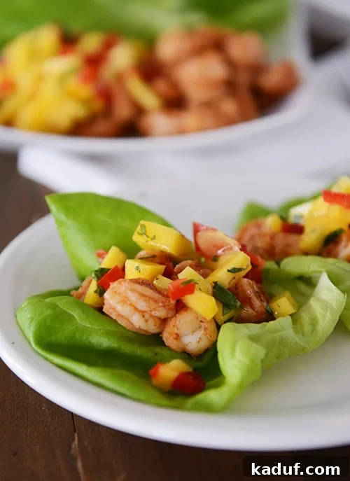 Tropical Shrimp Mango Lettuce Wraps 2 Vibrant shrimp and mango lettuce wraps artfully arranged on a pristine white plate, showcasing their fresh ingredients.