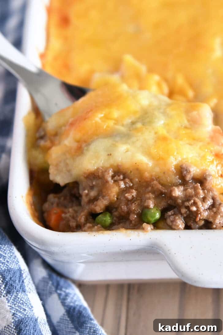 Lamb and Potato Comfort 2 A serving of classic Shepherd's Pie being scooped from a white casserole dish, showcasing the golden mashed potato topping and rich meat filling.
