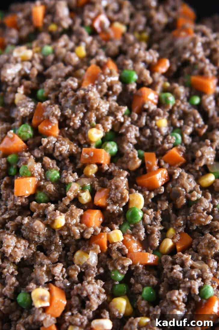 Lamb and Potato Comfort 3 A close-up view of the rich, cooked ground beef and vegetable mixture for Shepherd's Pie, simmering in a skillet.
