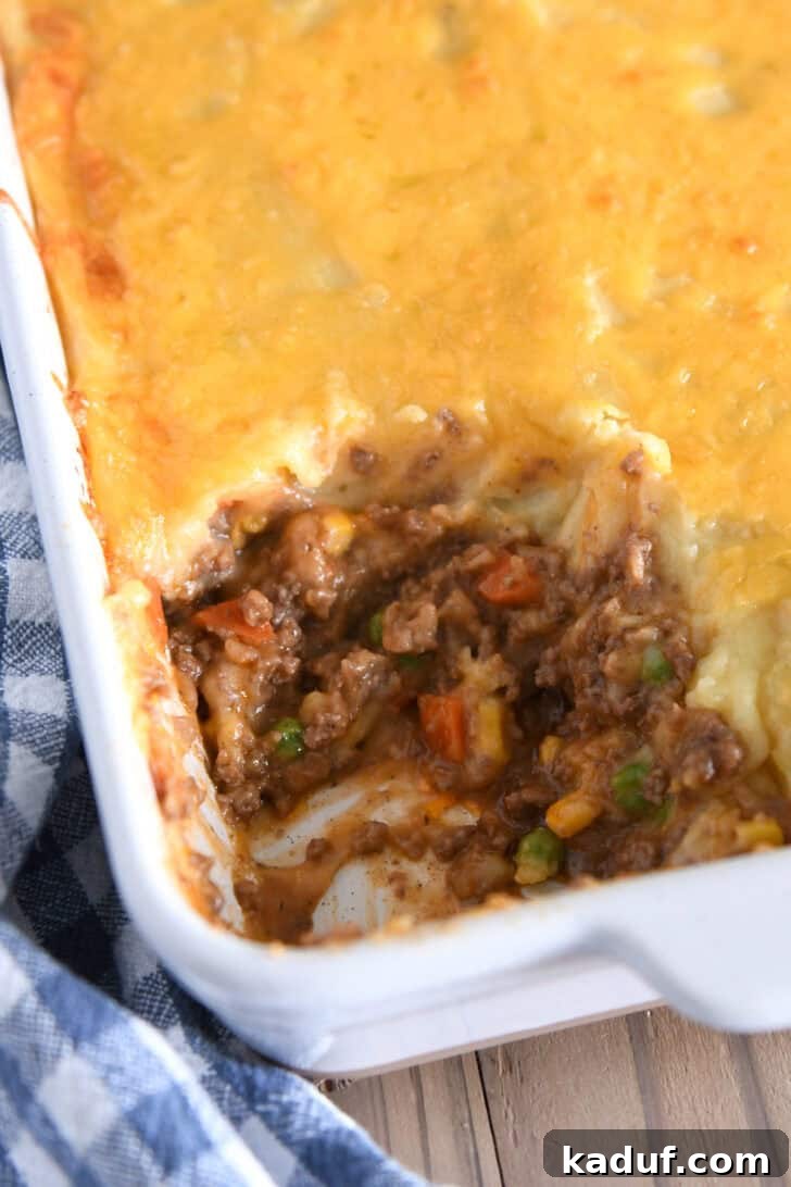 Lamb and Potato Comfort 7 A white casserole dish of classic Shepherd's Pie with a portion scooped out, revealing the layers of meat, vegetables, and mashed potatoes.