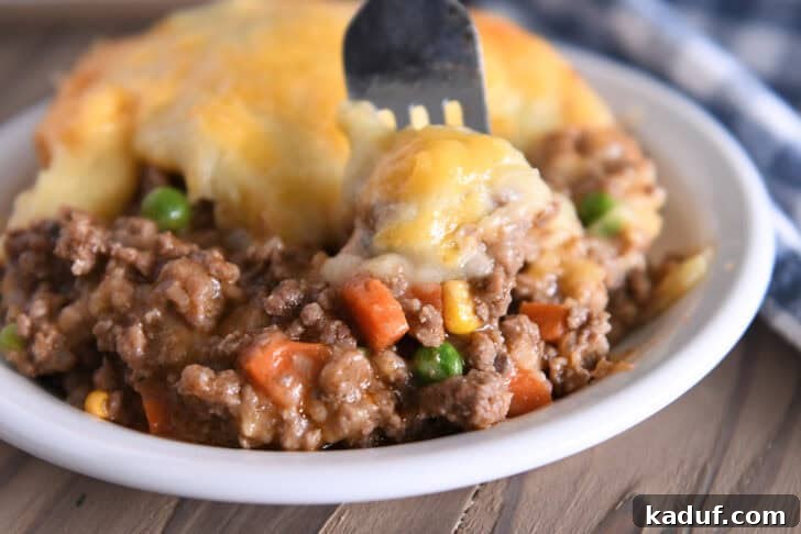 Lamb and Potato Comfort 9 A fork taking a bite from a serving of Shepherd's Pie in a white bowl, showing the layered perfection of meat, vegetables, and cheesy potatoes.