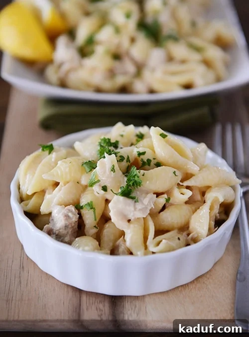 Effortless Creamy Tuna Pasta 2 A small white ramekin with cooked pasta and tuna and a platter of more behind it, showcasing a creamy and inviting texture.