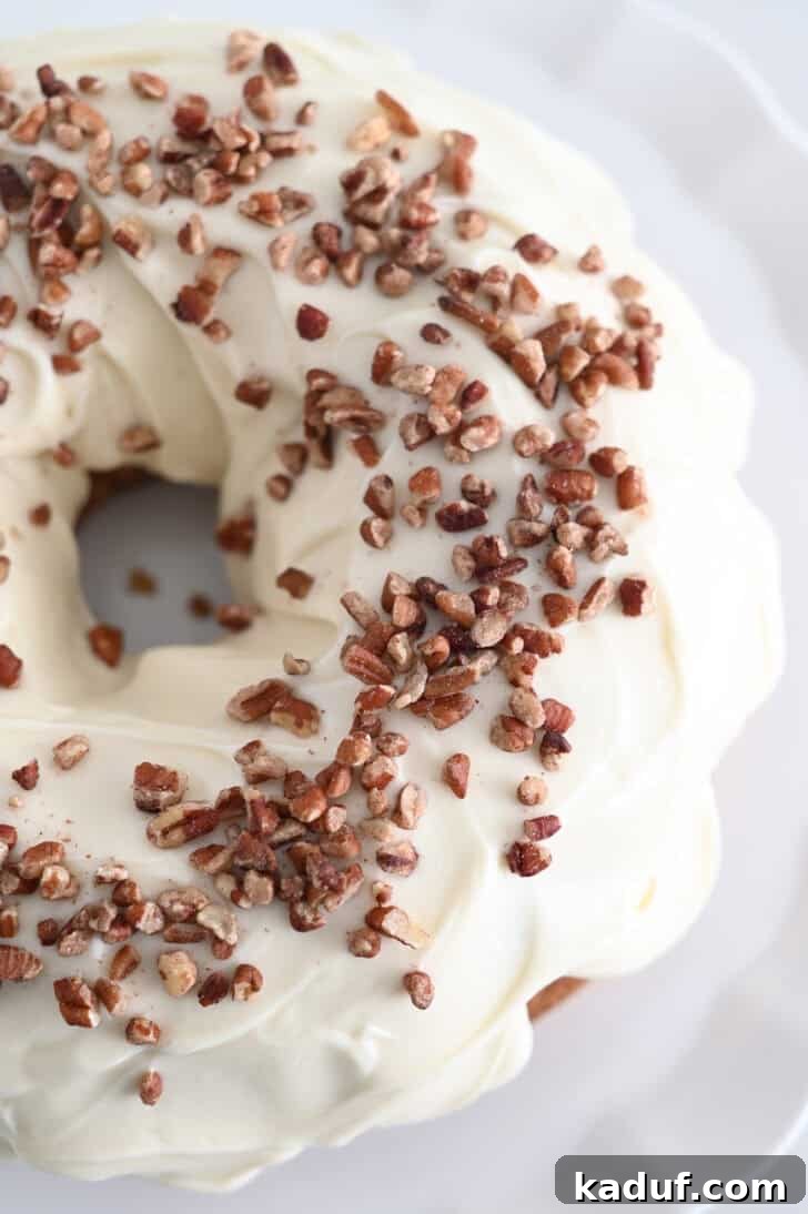 Marbled Carrot Bundt with Cream Cheese Bliss 11 A carrot cake bundt cake covered in white frosting and sprinkled with chopped pecans on a white place.