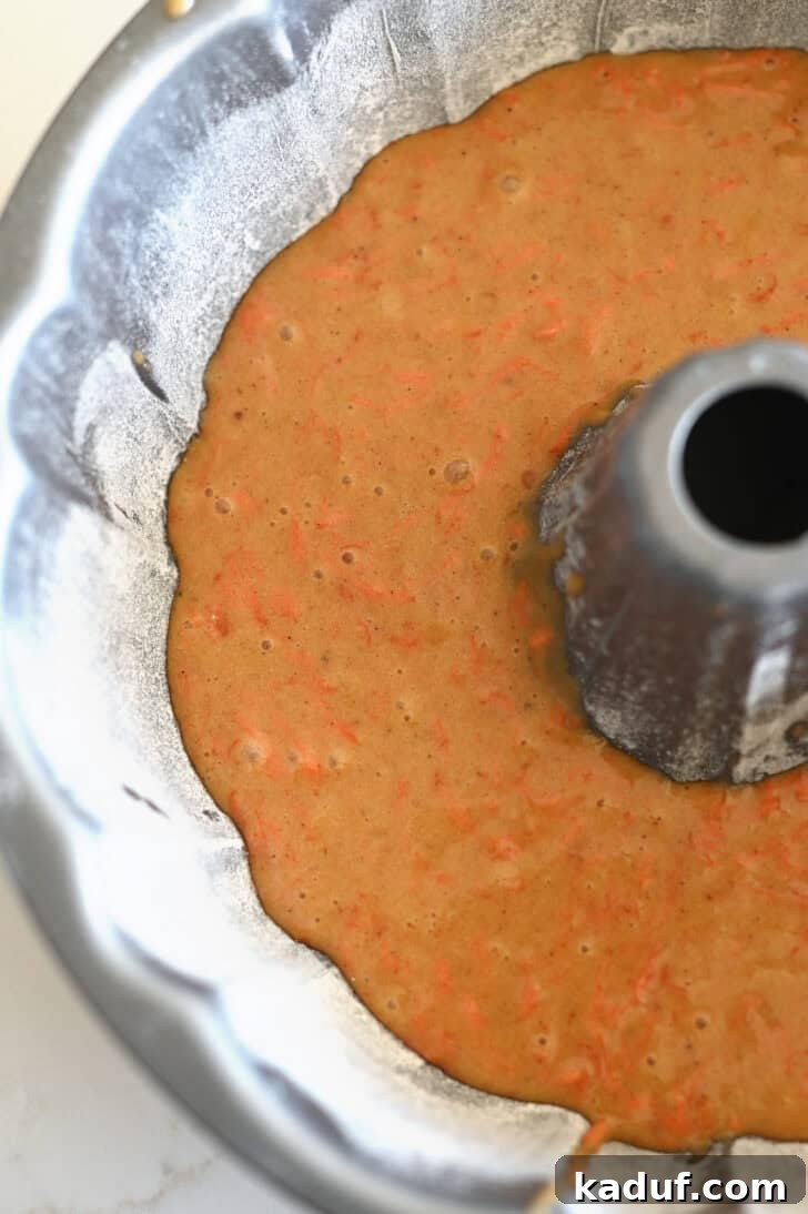 Marbled Carrot Bundt with Cream Cheese Bliss 7 Top down view of a greased and floured metal bundt pan with raw carrot cake batter inside.