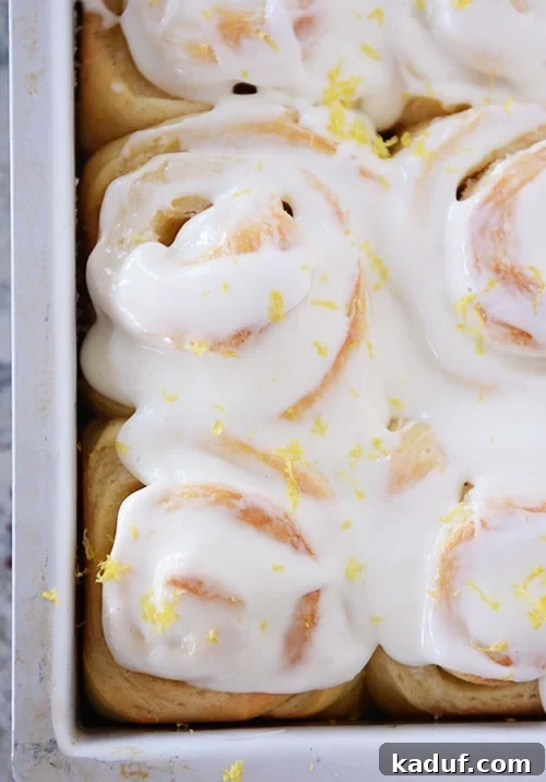 Gooey Lemon Rolls with Zesty Cream Cheese Glaze 2 Lemon sticky buns with glaze and lemon zest in metal pan.