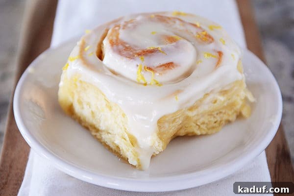Gooey Lemon Rolls with Zesty Cream Cheese Glaze 4 Whole frosted lemon sticky bun on white plate.