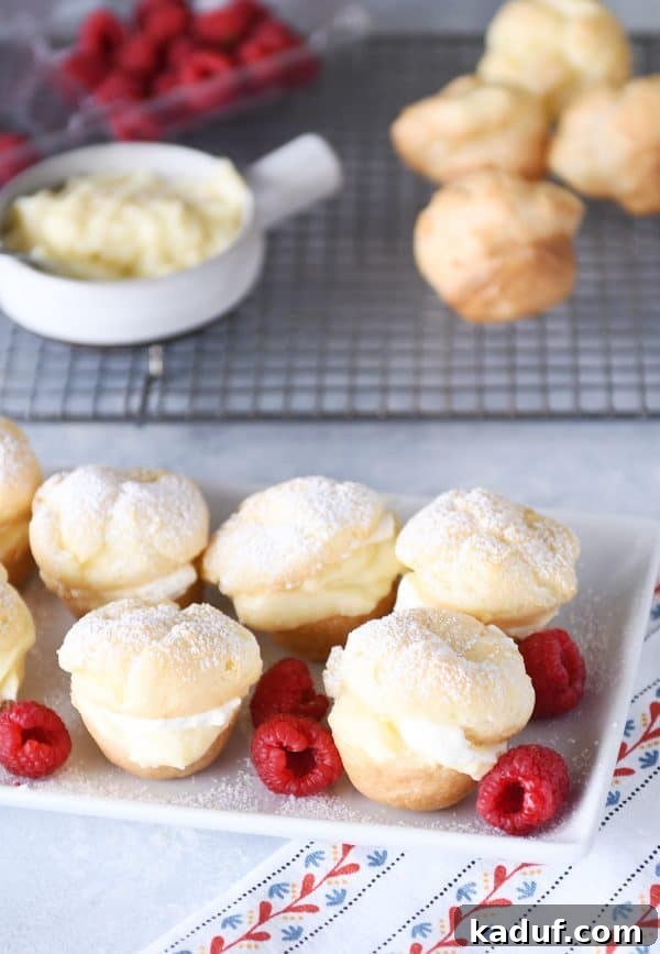 Effortless Cream Puff Perfection 2 A white tray filled with perfectly baked mini foolproof cream puffs, garnished with fresh red raspberries.
