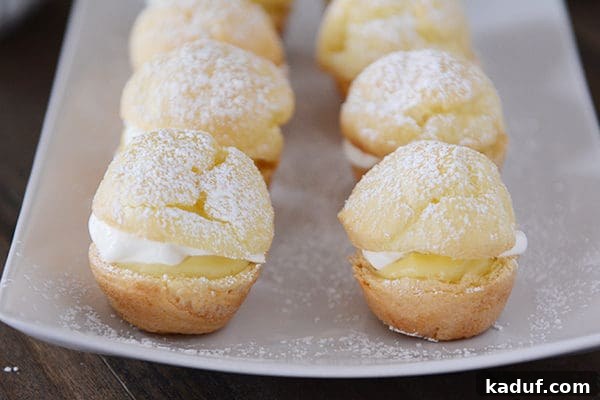 Effortless Cream Puff Perfection 8 A white platter adorned with numerous powdered sugar-dusted mini cream puffs, ready to be served.