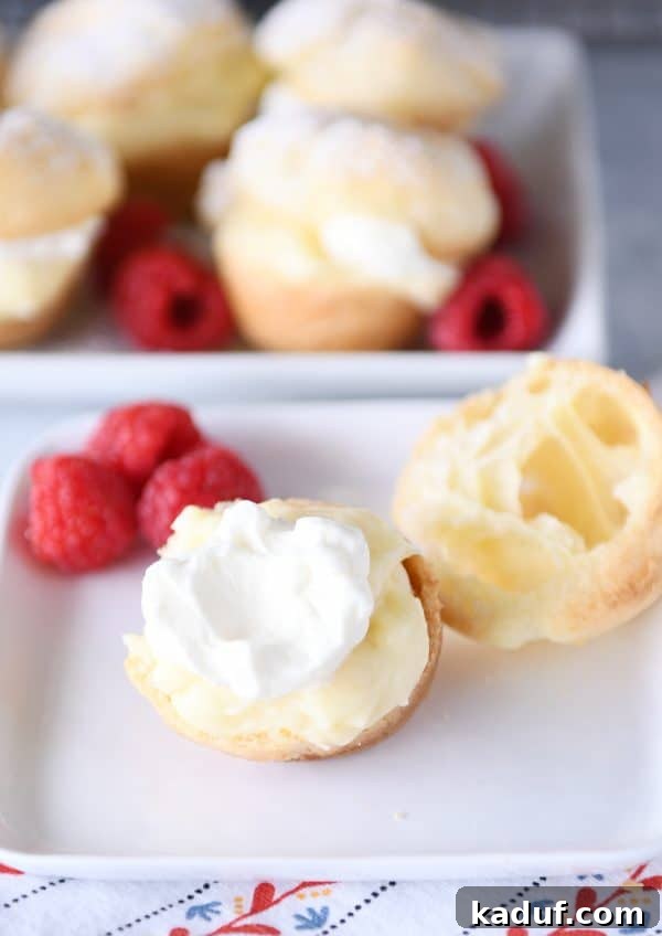 Effortless Cream Puff Perfection 3 A mini cream puff split open on a white plate, revealing a rich vanilla cream filling and topped with fresh raspberries.
