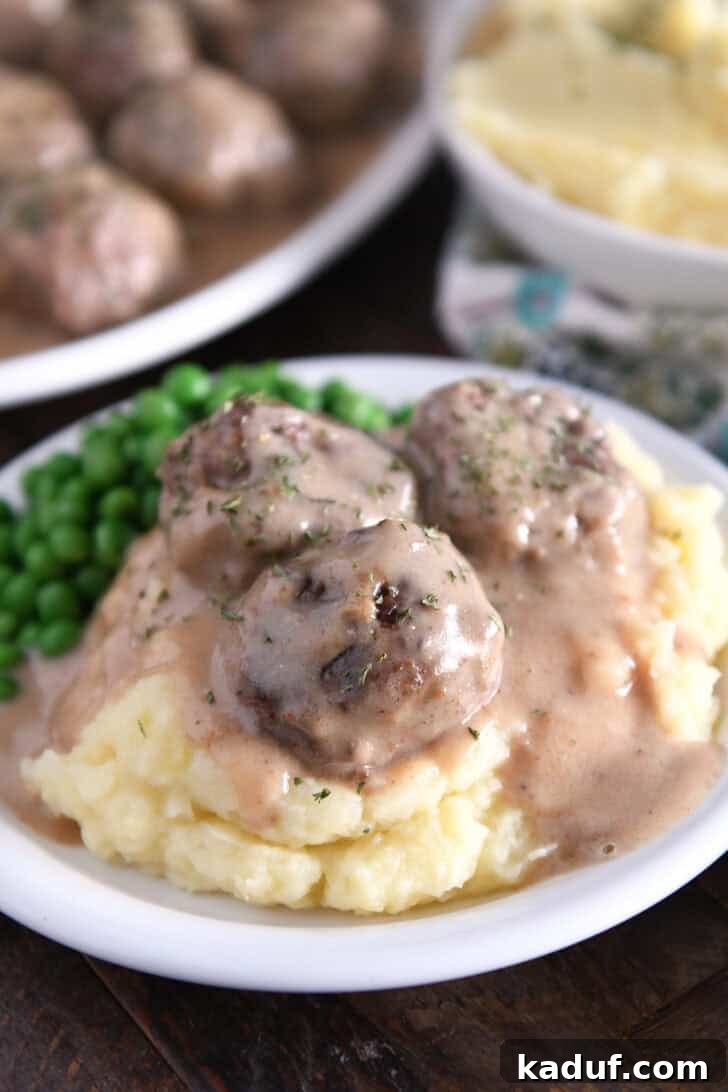 Creamy Skillet Swedish Meatballs 2 Three golden-brown Swedish meatballs resting on a bed of creamy mashed potatoes, generously coated in a rich, dark brown gravy, ready to be enjoyed.