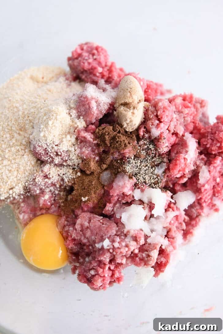 Creamy Skillet Swedish Meatballs 3 Glass bowl showcasing a mix of ground beef, finely grated onion, an egg, pepper, a dash of nutmeg, brown sugar, and breadcrumbs, ready for meatball preparation.