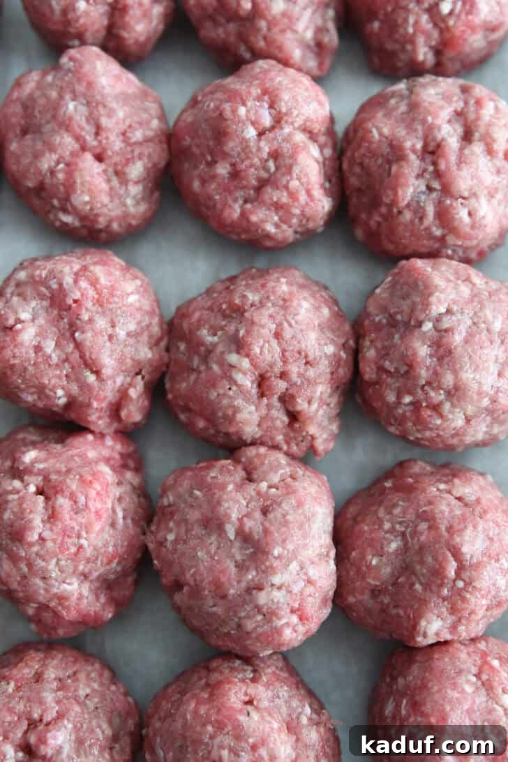Creamy Skillet Swedish Meatballs 4 A top-down view of nine perfectly formed, unbaked Swedish meatballs arranged neatly on parchment paper, awaiting their skillet transformation.