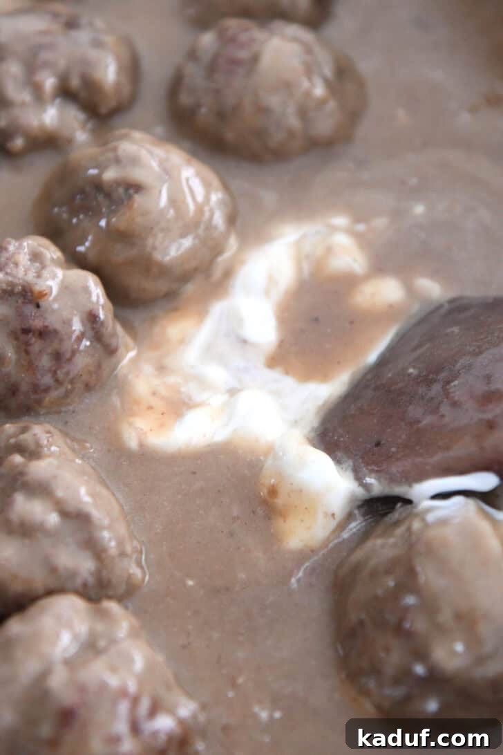 Creamy Skillet Swedish Meatballs 8 A spoonful of creamy sour cream being gently incorporated into the rich brown sauce, adding a velvety texture and tangy finish to the Swedish meatballs.