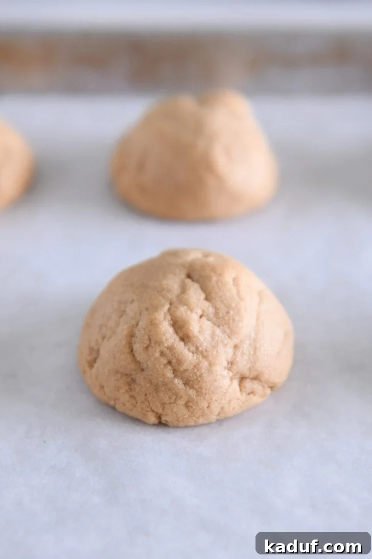 Irresistible Peanut Butter Cookies 7 Freshly baked puffy peanut butter cookie on white parchment paper, ready for the pressing technique.