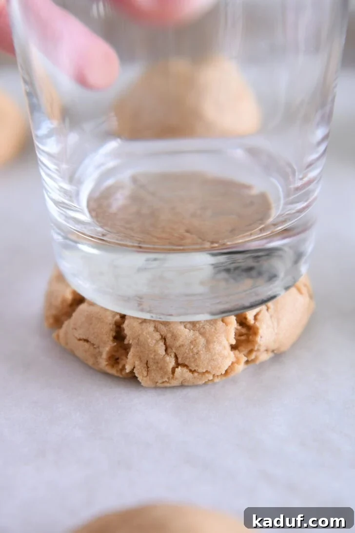 Irresistible Peanut Butter Cookies 8 Hands pressing a warm peanut butter cookie flat with the bottom of a glass, demonstrating the secret technique.