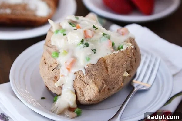 Loaded Chicken Pot Pie Spud 4 A golden-brown baked potato, split open and piled high with a steaming, creamy chicken pot pie filling, ready to be enjoyed.