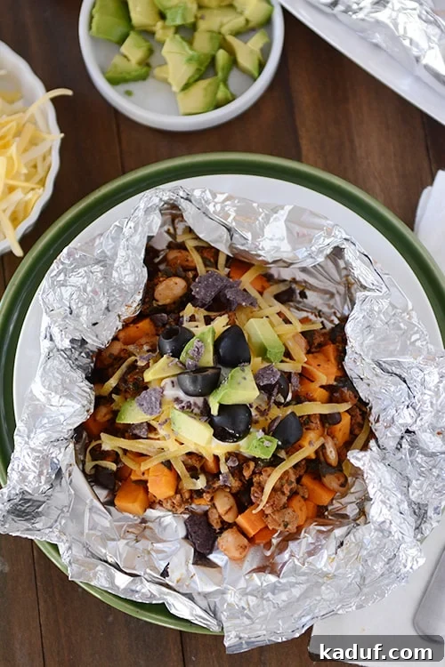 Foil Roasted Sweet Potato Tacos 2 Top view of a tinfoil packet of a cooked sweet potato taco mixture topped with cheese, avocado and sliced olives. A truly delicious and healthy sweet potato taco foil packet meal.