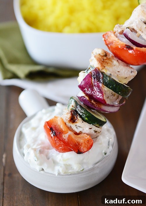 Juicy Greek Chicken Skewers with Refreshing Tzatziki 5 A greek chicken kebab getting dipped into a bowl of sauce.