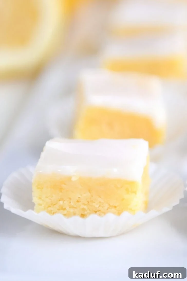Mini Lemon Brownie Delights 7 A line of lemon brownie squares topped with a white glaze in white muffin cups on a white serving platter, beautifully arranged for presentation at an event.