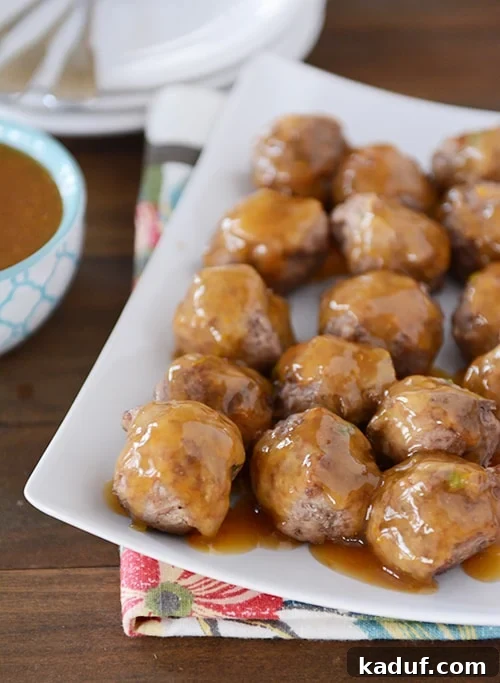 Sticky Zesty Orange Meatballs 2 A white platter with cooked meatballs covered in an orange glaze.