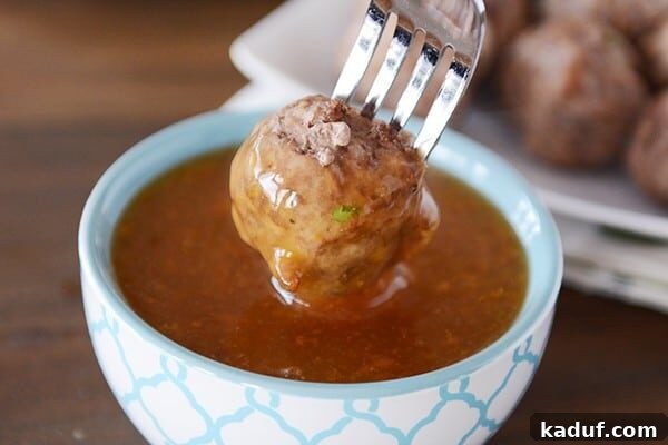 Sticky Zesty Orange Meatballs 3 A cooked meatball getting dipped into a bowl of orange sauce.