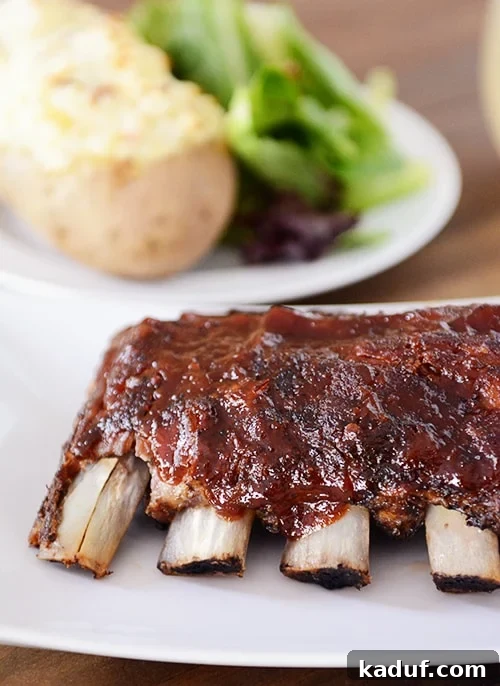 Root Beer Glazed Slow Cooker Baby Back Ribs 2 A rack of slow cooker baby back ribs smothered in homemade root beer BBQ sauce on a white platter, served with a side of roasted potatoes and a fresh green salad.