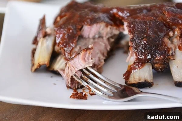 Root Beer Glazed Slow Cooker Baby Back Ribs 3 A fork piercing a piece of tender slow cooker baby back rib, showcasing the juicy meat and glistening root beer BBQ sauce.
