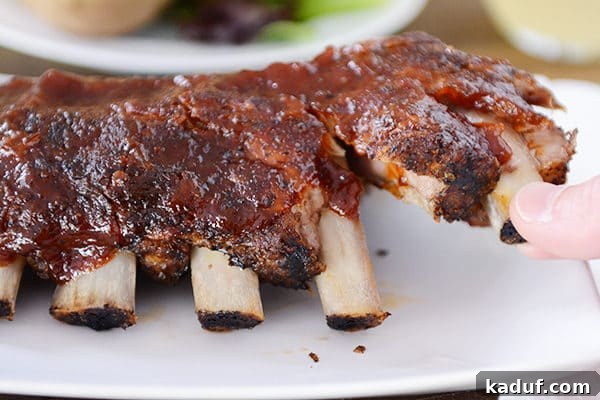 Root Beer Glazed Slow Cooker Baby Back Ribs 4 Two extremely tender ribs being easily pulled apart from a cooked rack, demonstrating the fall-off-the-bone quality achieved in the slow cooker.