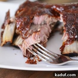 Close-up of a fork taking a bite out of a tender slow cooker baby back rib, highlighted by the homemade root beer BBQ sauce.