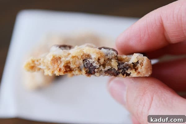 Soft Chewy Seven Layer Cookies Individual Perfection 3 A close-up view of the irresistible, gooey interior of a half-eaten 7-layer cookie, showcasing melted chocolate and butterscotch chips amidst the soft cookie dough.