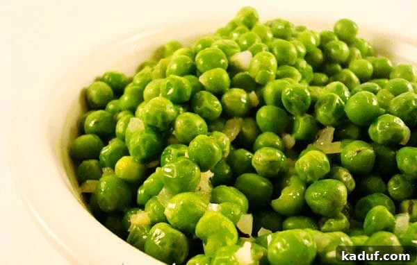 Thyme-Kissed Butter Peas 3 Close-up shot of vibrant green peas tossed with minced garlic cloves and fresh thyme sprigs in a white bowl.