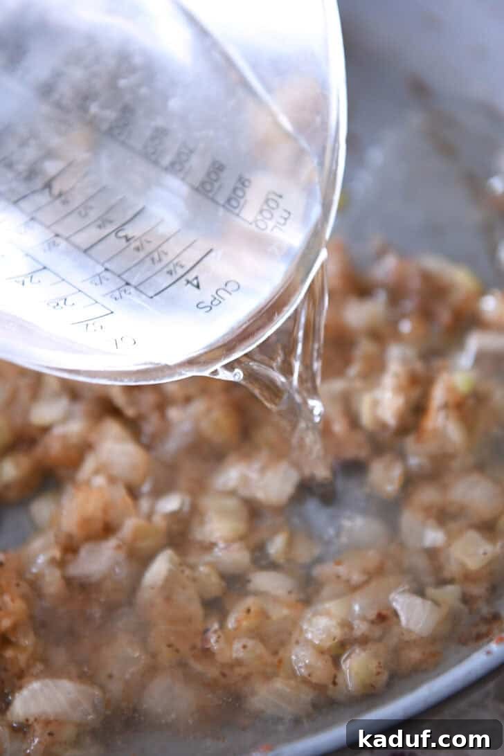Rustic German Potato Salad 5 A liquid measuring cup pouring water into a skillet with browned onion pieces, illustrating the process of adding liquids to the developing dressing.