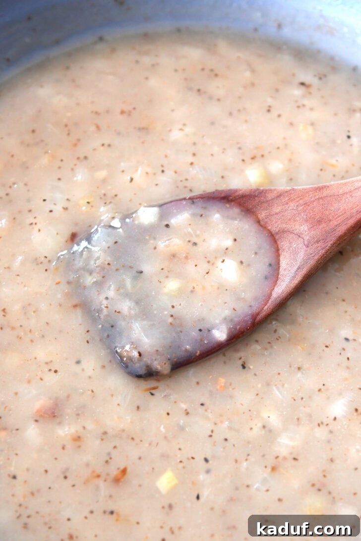Rustic German Potato Salad 6 A wooden spoon in a skillet full of a white onion sauce, showing the thickened and creamy consistency of the finished German potato salad dressing.