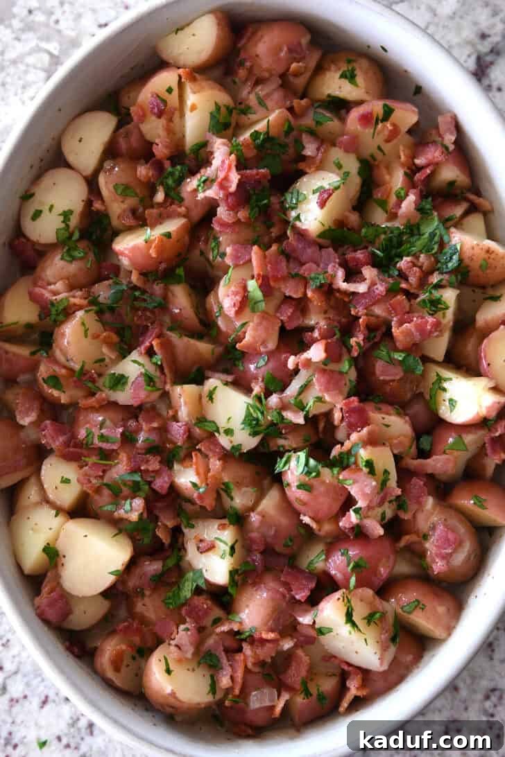 Rustic German Potato Salad 8 Top down view of a white oval dish with potato chunks, crispy bacon pieces, and fresh chopped parsley, showcasing the beautifully assembled German Potato Salad.
