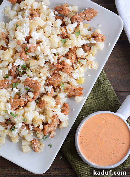 Vibrant Roasted Red Pepper Pesto Hash Browns 2 Top down view of a white tray of cubed potatoes and sausage next to a bowl of red pepper sauce.