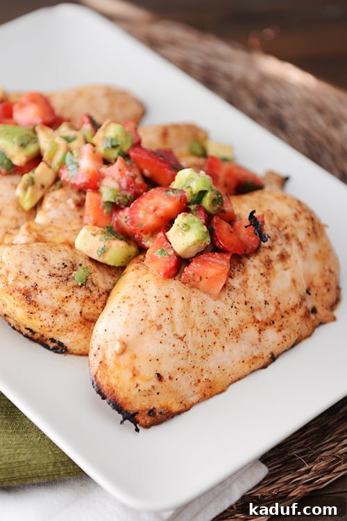 A white tray of grilled chicken breasts topped with strawberry-avocado salsa.