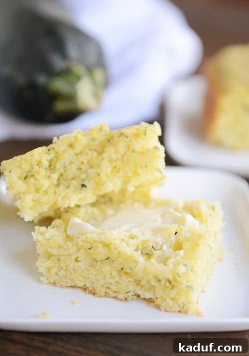 Golden Zucchini Cornbread 2 A big piece of fluffy zucchini cornbread cut in half with butter on one half, showcasing its moist texture.
