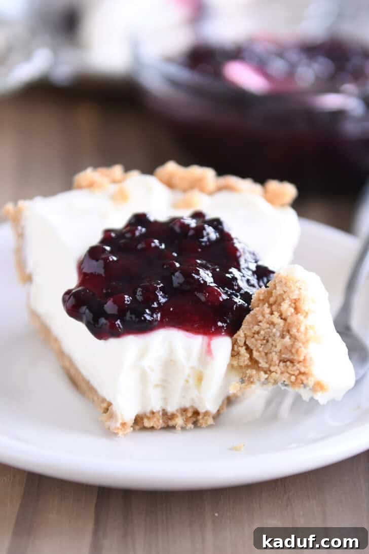 Ultimate No-Bake Cheesecake 2 A slice of creamy no-bake cheesecake with a vibrant dollop of blueberry sauce on top, presented on a pristine white plate. A fork rests beside the slice, holding a perfect bite of the cheesecake, inviting you to taste.